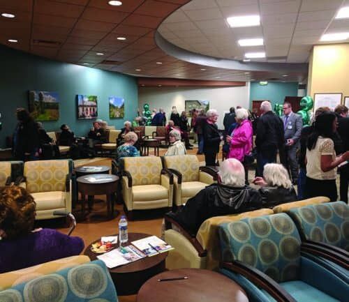 People gathering in modern hospital lobby with comfortable seating and artwork during open house event.
