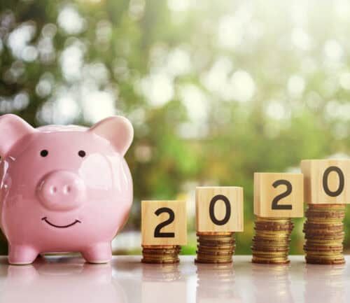 Pink piggy bank next to stacked coins with wooden blocks spelling "2020"