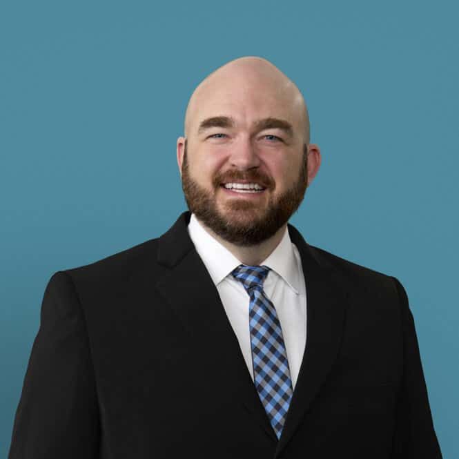 Professional headshot of Andrew Costerisan, PA-C in dark suit with blue checkered tie