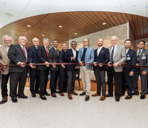 Group of men in business attire cutting red ribbon at healthcare facility opening ceremony