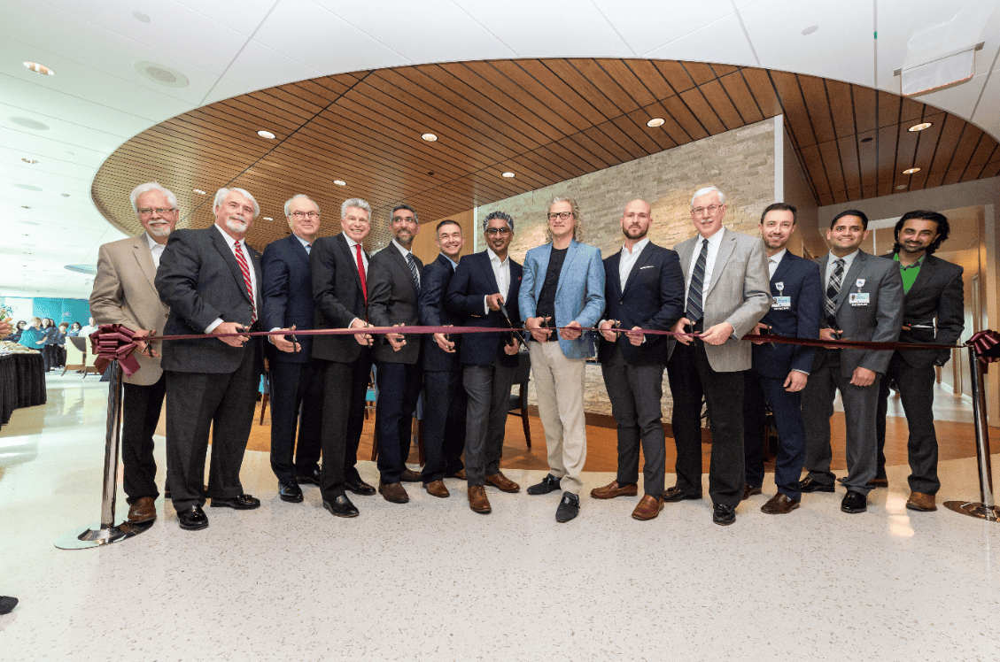 Group of men in business attire cutting red ribbon at healthcare facility opening ceremony