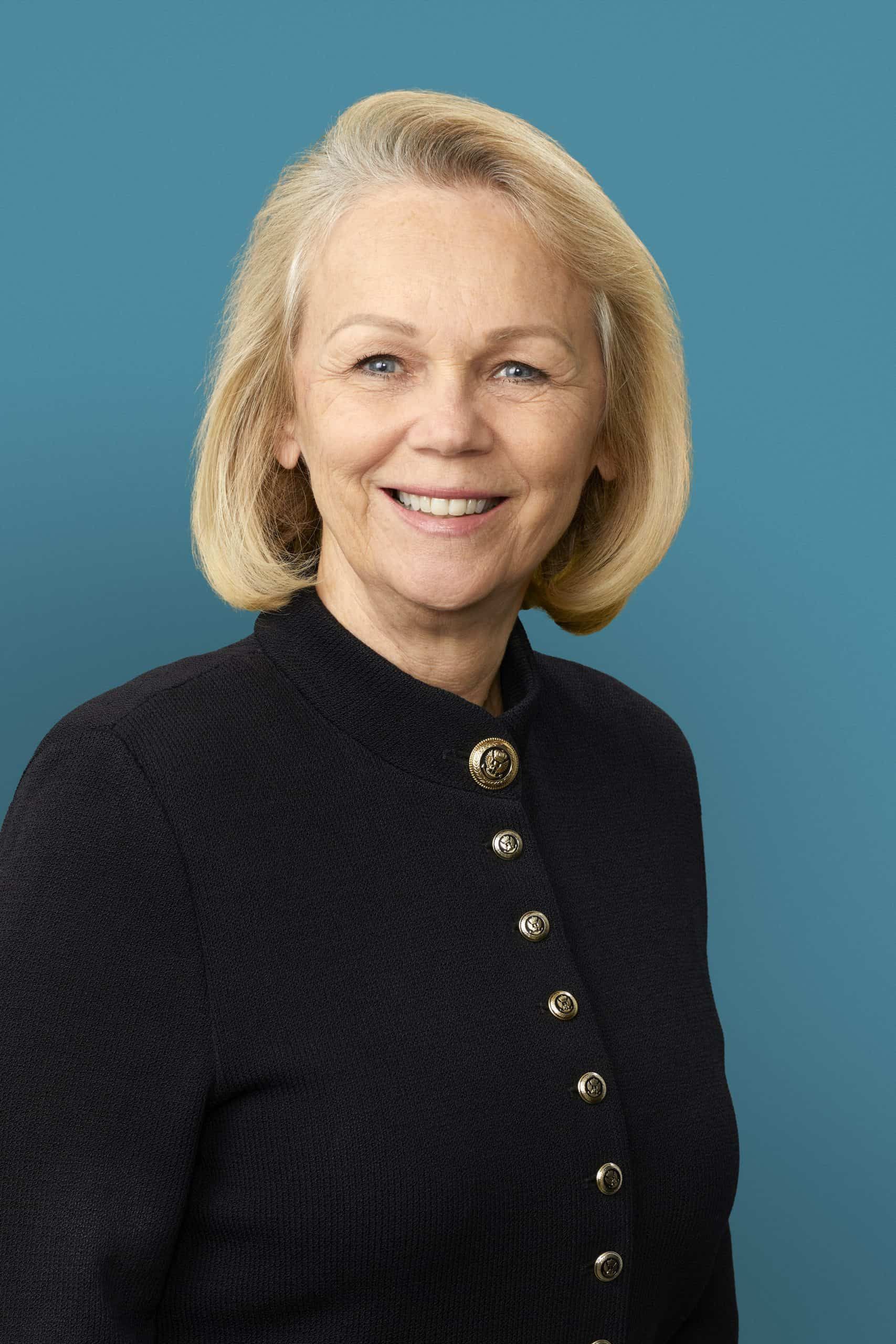 Professional headshot of woman in black cardigan with gold buttons smiling warmly