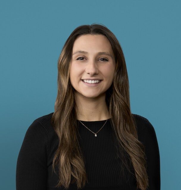 Professional headshot of Camille Hughes, PA-C smiling in black sweater against blue background