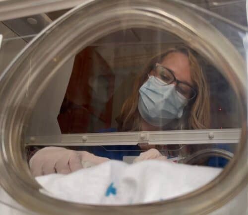 Healthcare worker in protective mask examining newborn baby in hospital incubator