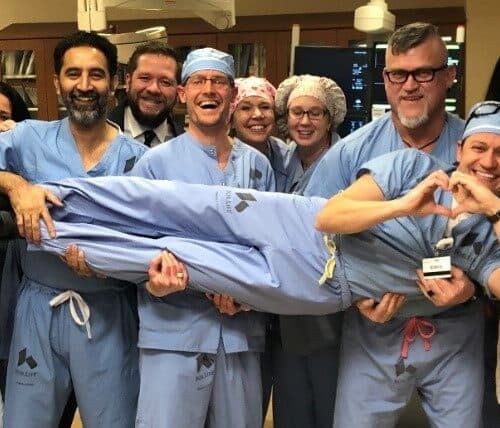 Medical team in scrubs celebrating together while carrying colleague in cardiac catheterization lab