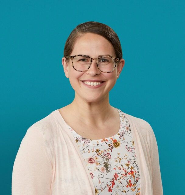 Professional headshot of Chelsea Brunsman, DO, smiling woman with glasses and floral top