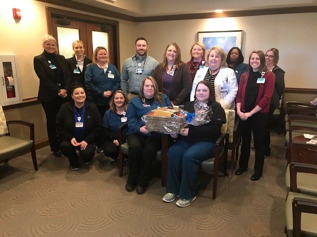Healthcare team members gathered together holding gift baskets in hospital waiting area
