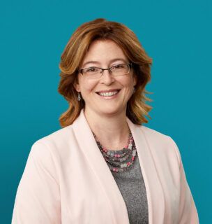 Professional headshot of Dr. Deanna M. Allgeyer smiling in white blazer against teal background