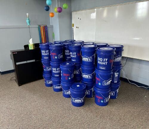 Multiple blue Lowe's emergency preparedness buckets stacked in classroom or office setting.