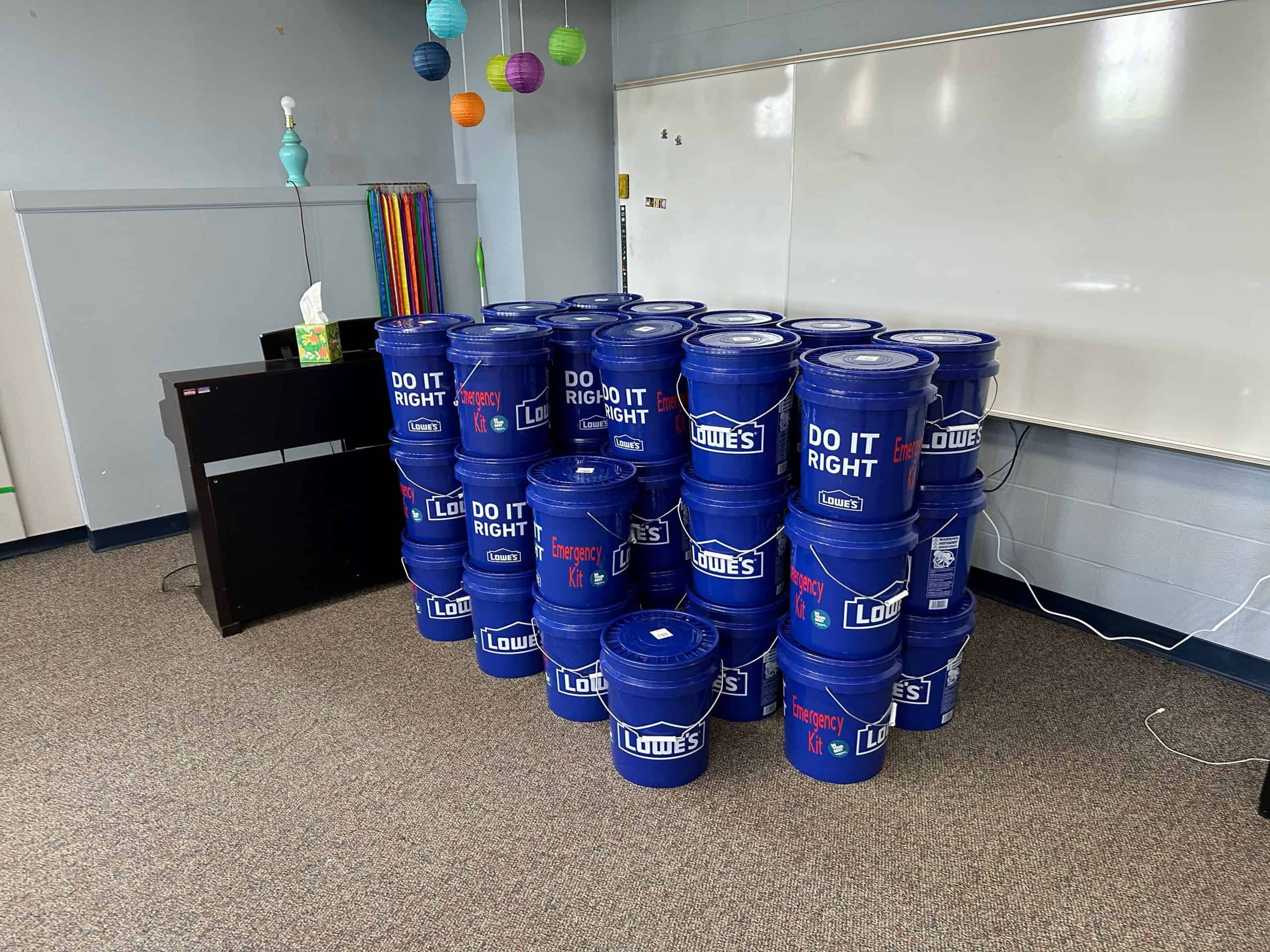Multiple blue Lowe's emergency preparedness buckets stacked in classroom or office setting.
