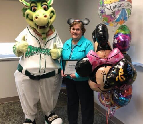 Dragon mascot and healthcare employee celebrating with congratulations balloons in office