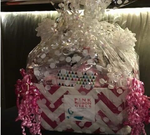 Gift basket wrapped in clear cellophane with pink ribbon and chevron pattern design.
