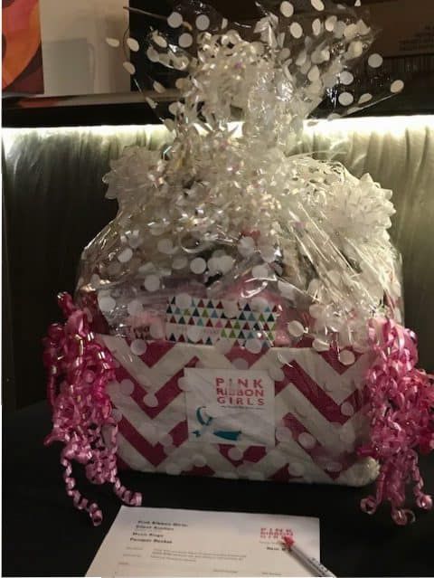 Gift basket wrapped in clear cellophane with pink ribbon and chevron pattern design.