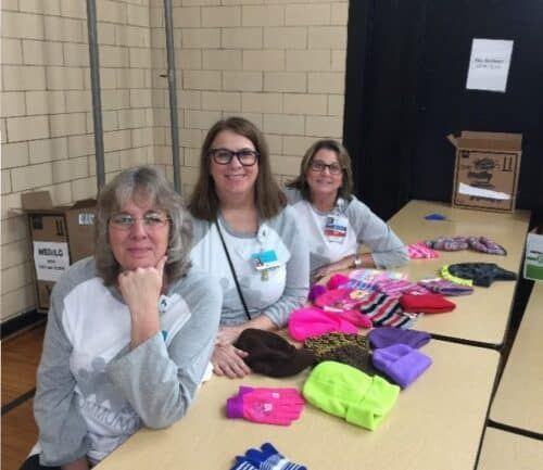 Three volunteers sorting colorful winter hats and gloves on table for donation drive