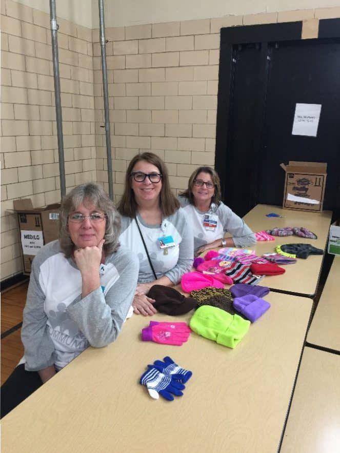 Three volunteers sorting colorful winter hats and gloves on table for donation drive