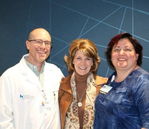 Three people posing together in hospital setting - doctor in white coat with two women