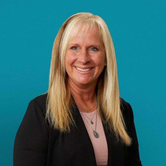 Professional headshot of Heidi Riley, APRN-CNP, smiling in black blazer against teal background