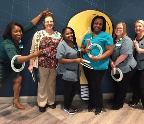 Six female healthcare workers celebrating Hospital Week with stethoscope props and awards