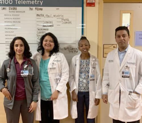 Four healthcare professionals in white coats posing together in hospital hallway