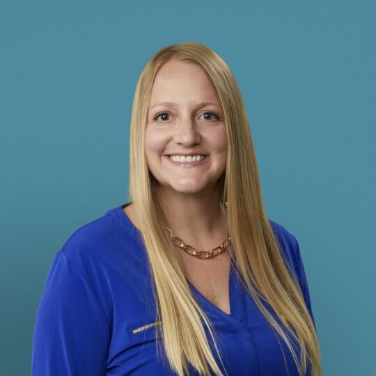 Professional headshot of Jaimie Kern, APRN-CNP in blue scrubs smiling at camera