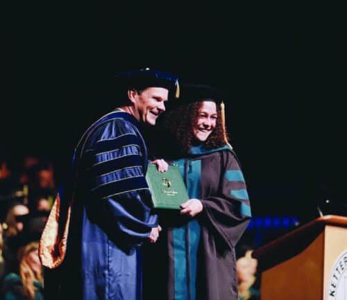 Two graduates in academic regalia shaking hands during Kettering College graduation ceremony