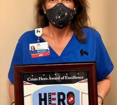 Healthcare worker holding Crisis Hero Award of Excellence certificate while wearing mask