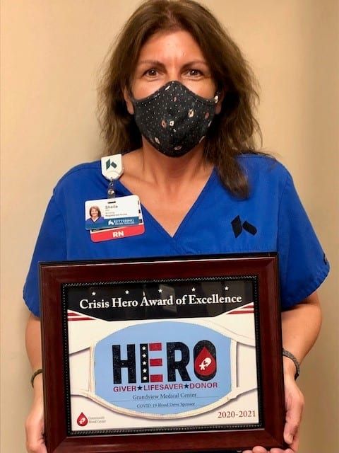 Healthcare worker holding Crisis Hero Award of Excellence certificate while wearing mask