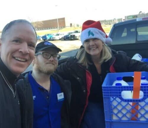 Three healthcare volunteers posing together with blue donation crates during community outreach event