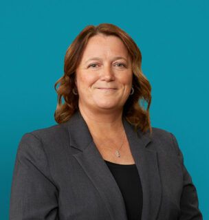 Professional headshot of Krista Miller, APRN-CNP in gray blazer against teal background