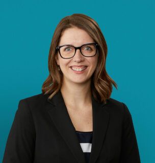 Professional headshot of Dr. Kristen Young smiling in black blazer against teal background