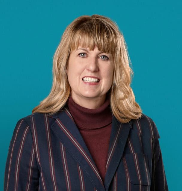 Professional headshot of Leslee A. Chavez, APRN-CNP in striped blazer against teal background