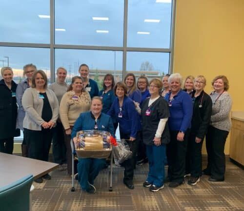 Healthcare team members gathered together celebrating with gift basket in bright conference room