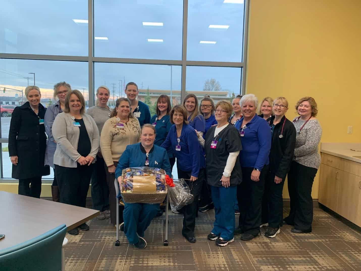 Healthcare team members gathered together celebrating with gift basket in bright conference room
