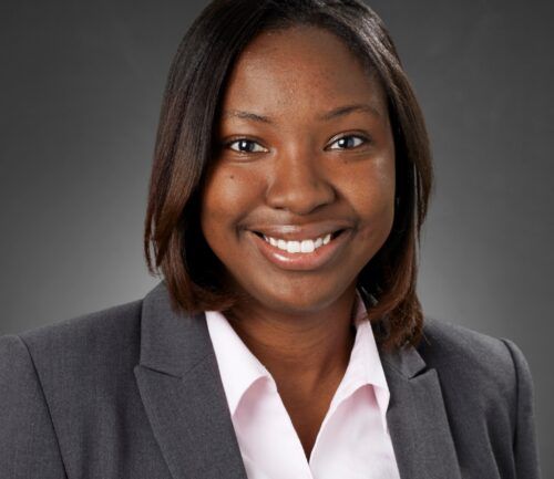 Professional headshot of Vimbai Mazani wearing gray blazer and white shirt, smiling