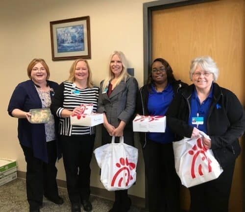 Five healthcare staff members holding gift bags and food containers during Medical Practice Week celebration.