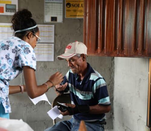 Healthcare worker in scrubs providing medical care to elderly patient in cap