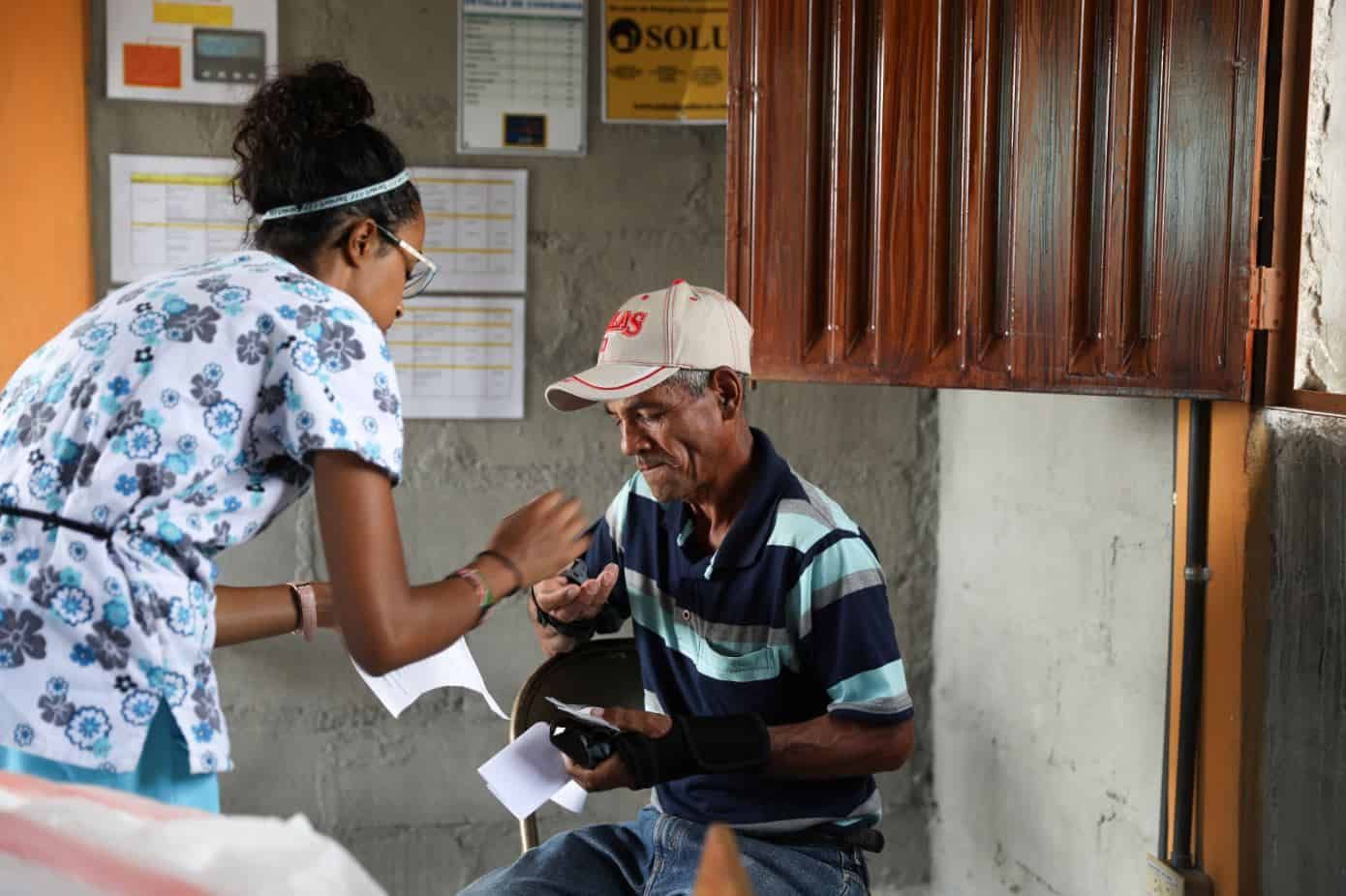 Healthcare worker in scrubs providing medical care to elderly patient in cap