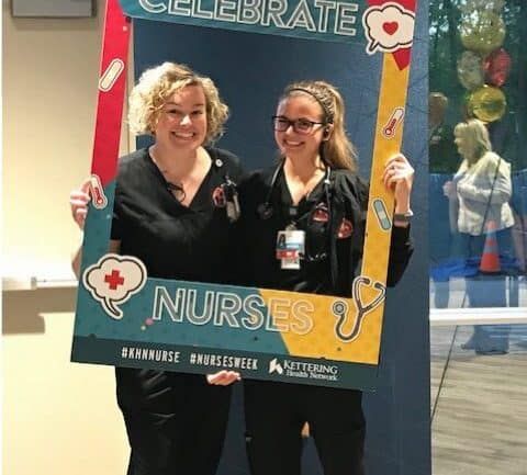 Two nurses posing with "It's Time to Celebrate Nurses" photo frame prop