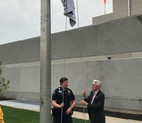 Two men raising a flag on a flagpole outside a medical building