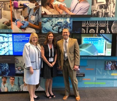 Three healthcare professionals posing together at medical conference display with quality care messaging