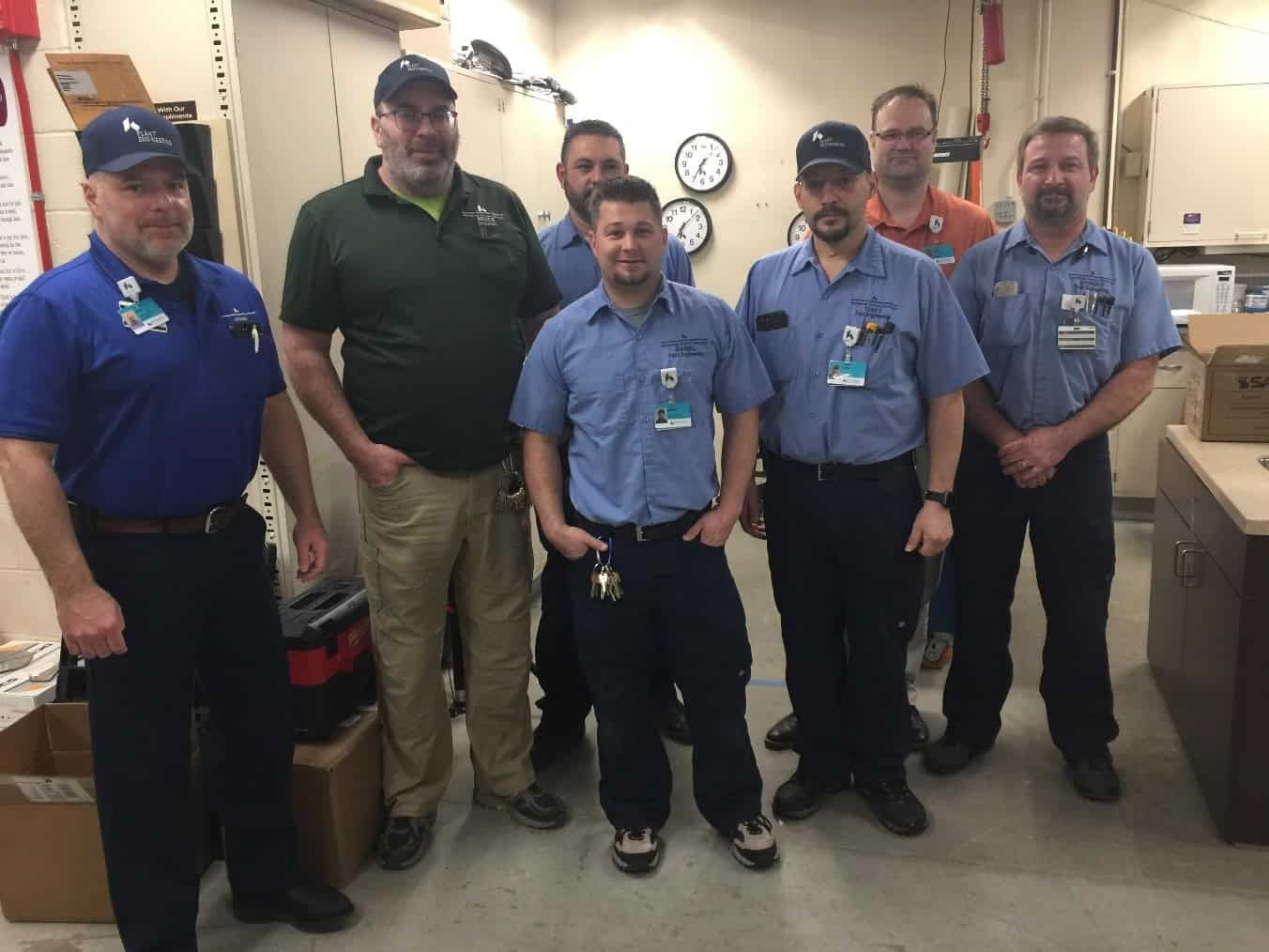 Seven Kettering Health plant engineering staff members posing together in maintenance workshop facility.