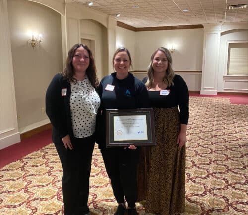 Three women celebrating with award certificate in elegant hotel conference room