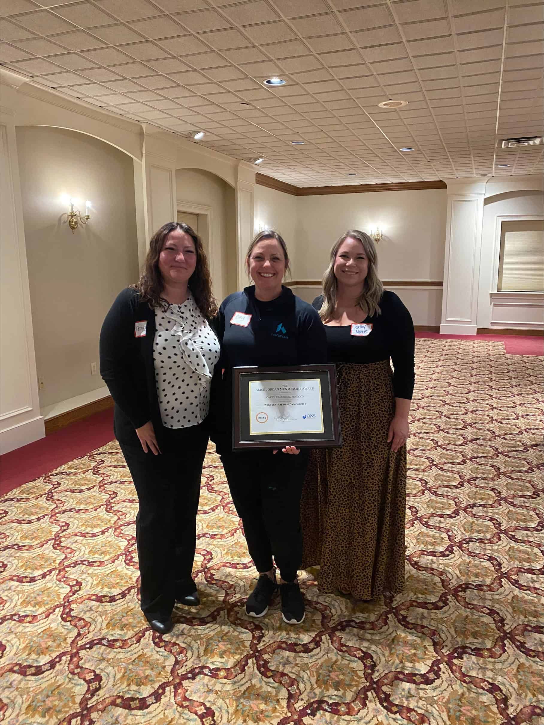 Three women celebrating with award certificate in elegant hotel conference room