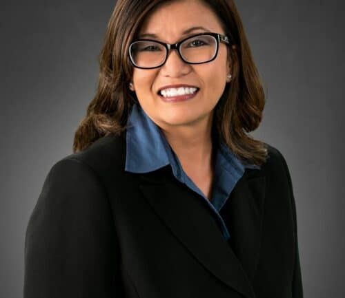 Professional headshot of woman in black blazer and blue shirt smiling at camera