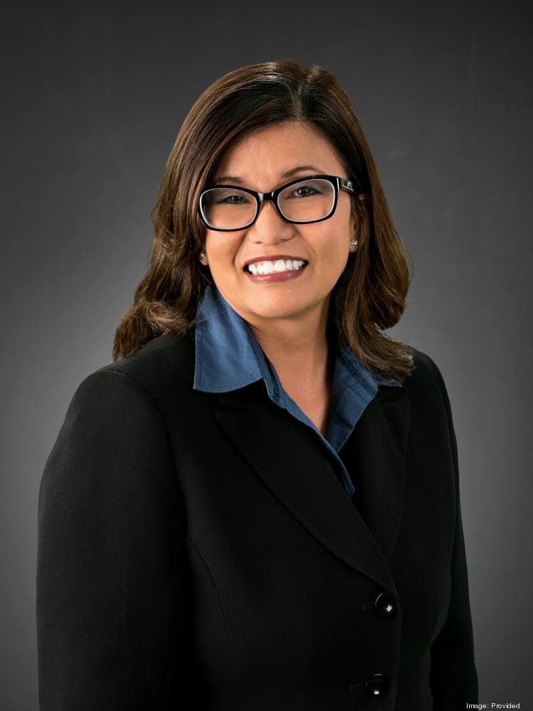 Professional headshot of woman in black blazer and blue shirt smiling at camera