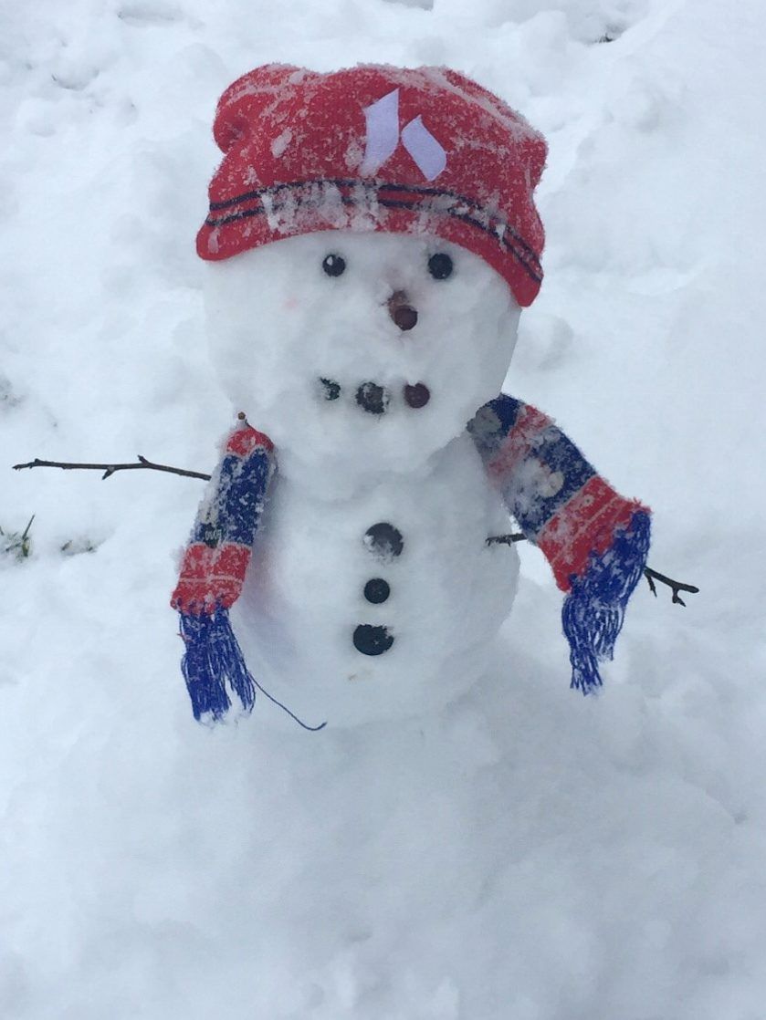 Snowman with red knit hat and blue striped scarf in snowy yard