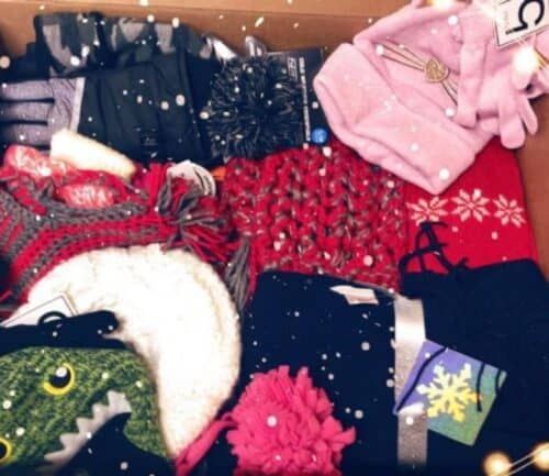 Cardboard box filled with colorful winter clothing and accessories surrounded by string lights