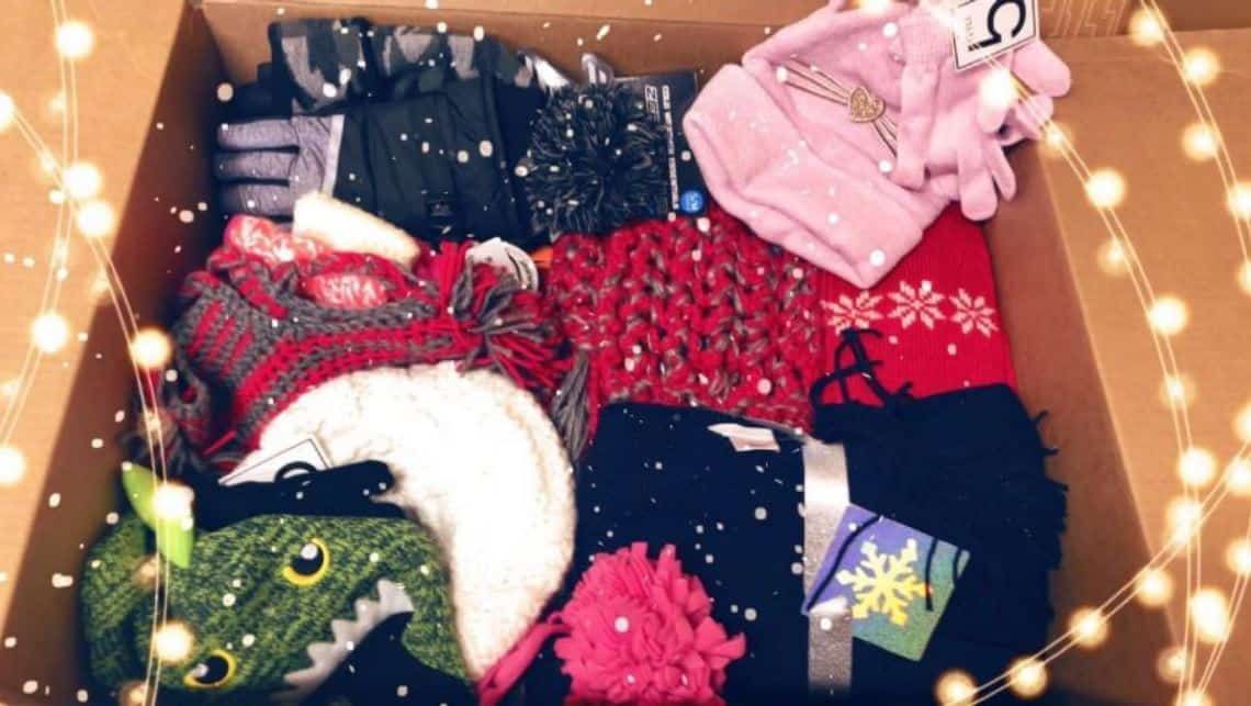 Cardboard box filled with colorful winter clothing and accessories surrounded by string lights