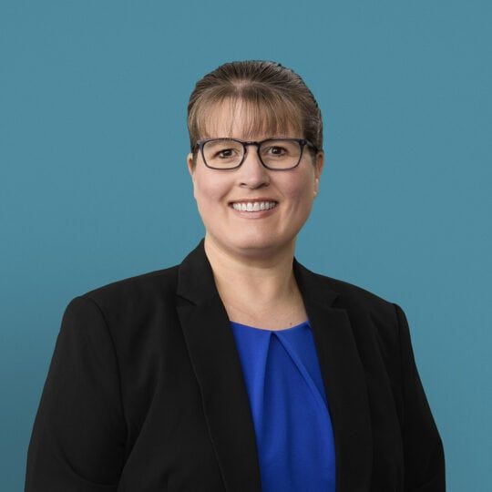 Professional headshot of Susen Wright, APRN-CNP, wearing glasses and black blazer with blue top