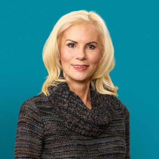 Professional headshot of Victoria Surdulescu, MD in gray sweater against teal background